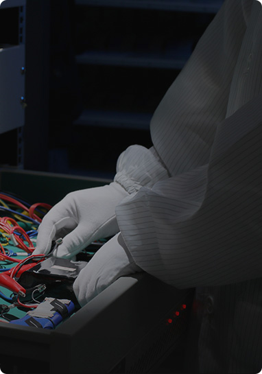 Technician in protective gloves and gown working on colorful wires inside electronic equipment.